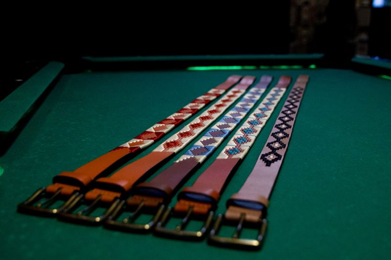 Five beaded leather belts laid out on green felt