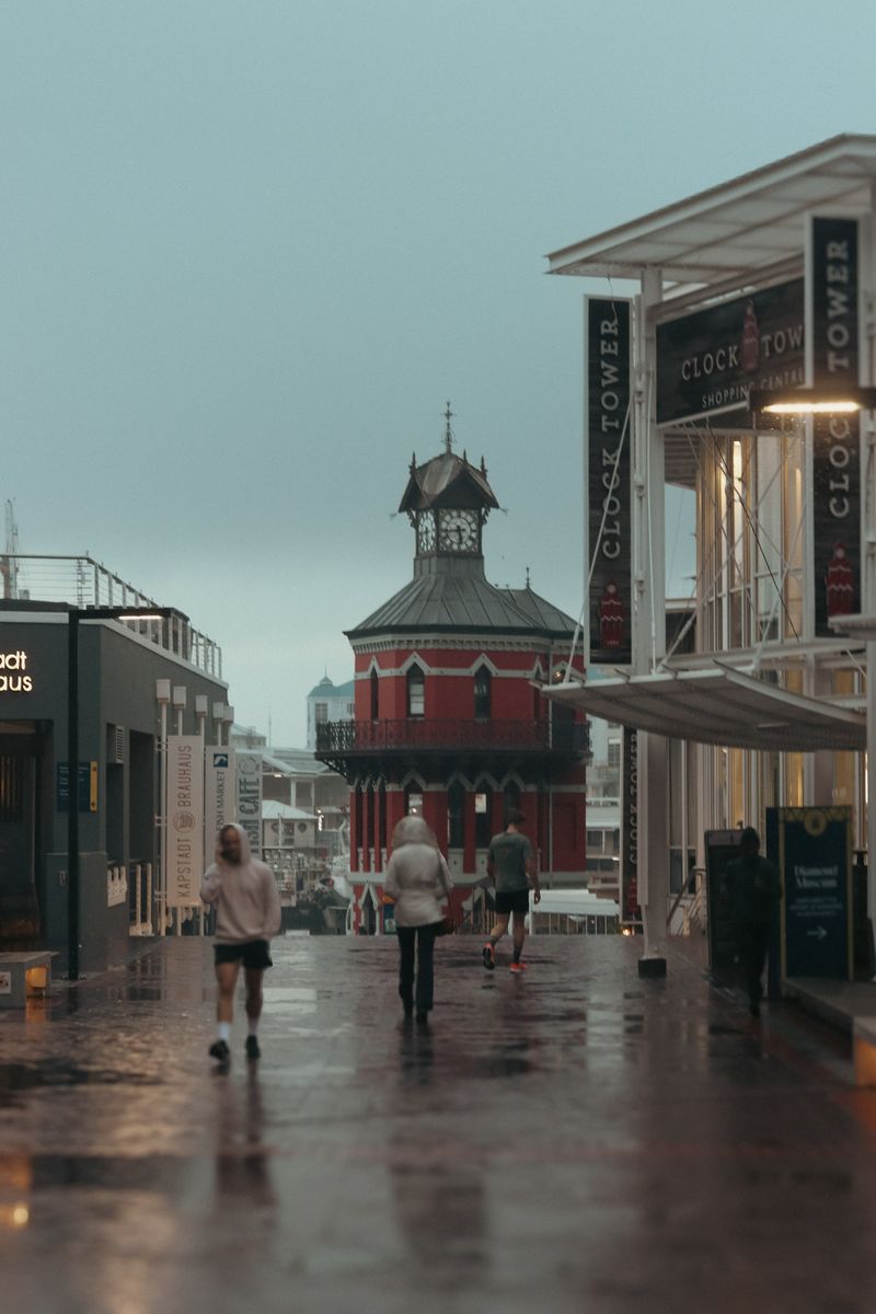 People walk a wet street toward a red clock tower