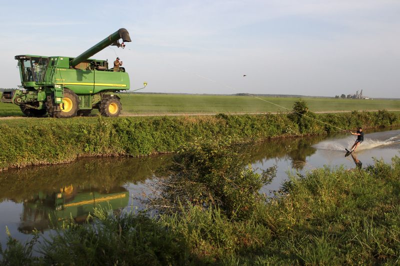 A combine on the field road pulls a wakeboarder down the farm ditch