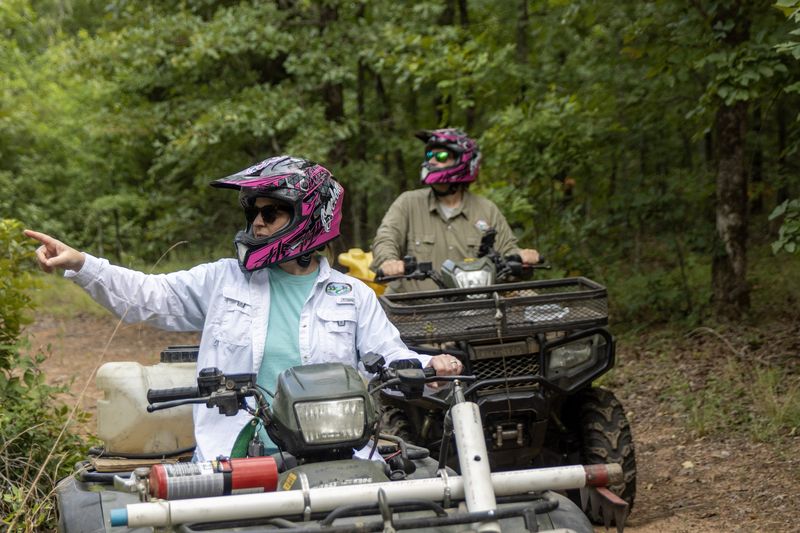 A field crew on ATVs in the woods, one rider pointing up the trail
