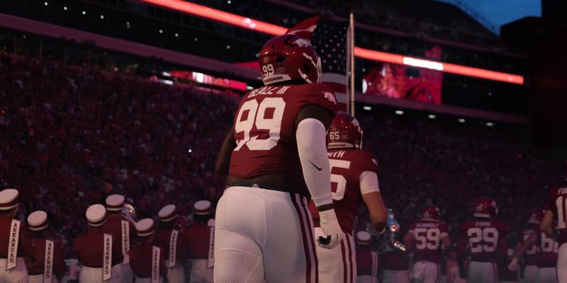 Football player number 99 walks to the field under red stadium lights