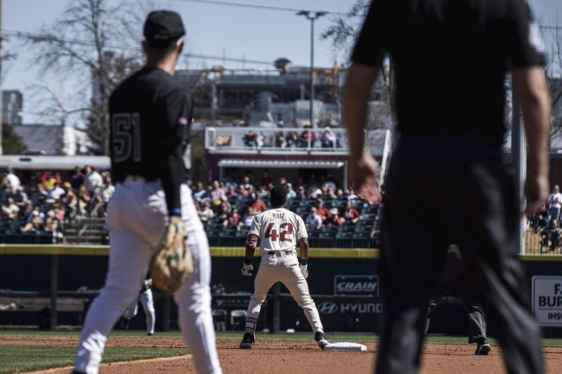 An infielder and an umpire watch a runner on base on a sunny afternoon