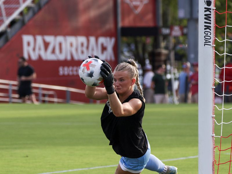 A soccer goalkeeper catches the ball in front of a Razorback sign